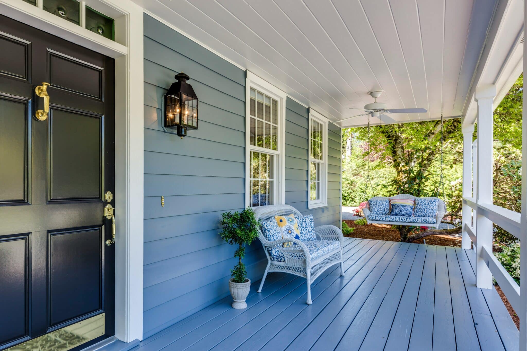 Well-maintained front porch with fresh paint, porch swing, and lush greenery